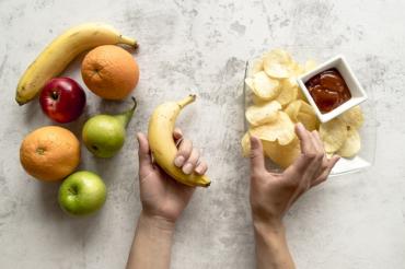 human-hand-holding-banana-potato-chips-cement-surface_23-2148193100.jpg